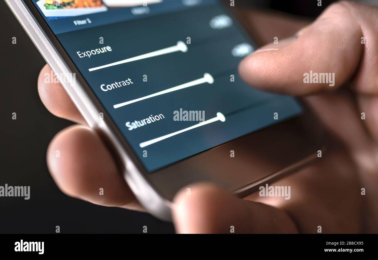 Modifica di foto con il telefono cellulare e la smart app. Man regolazione cursori. Modifica, manipolazione, miglioramento o miglioramento delle immagini con lo smartphone. Foto Stock