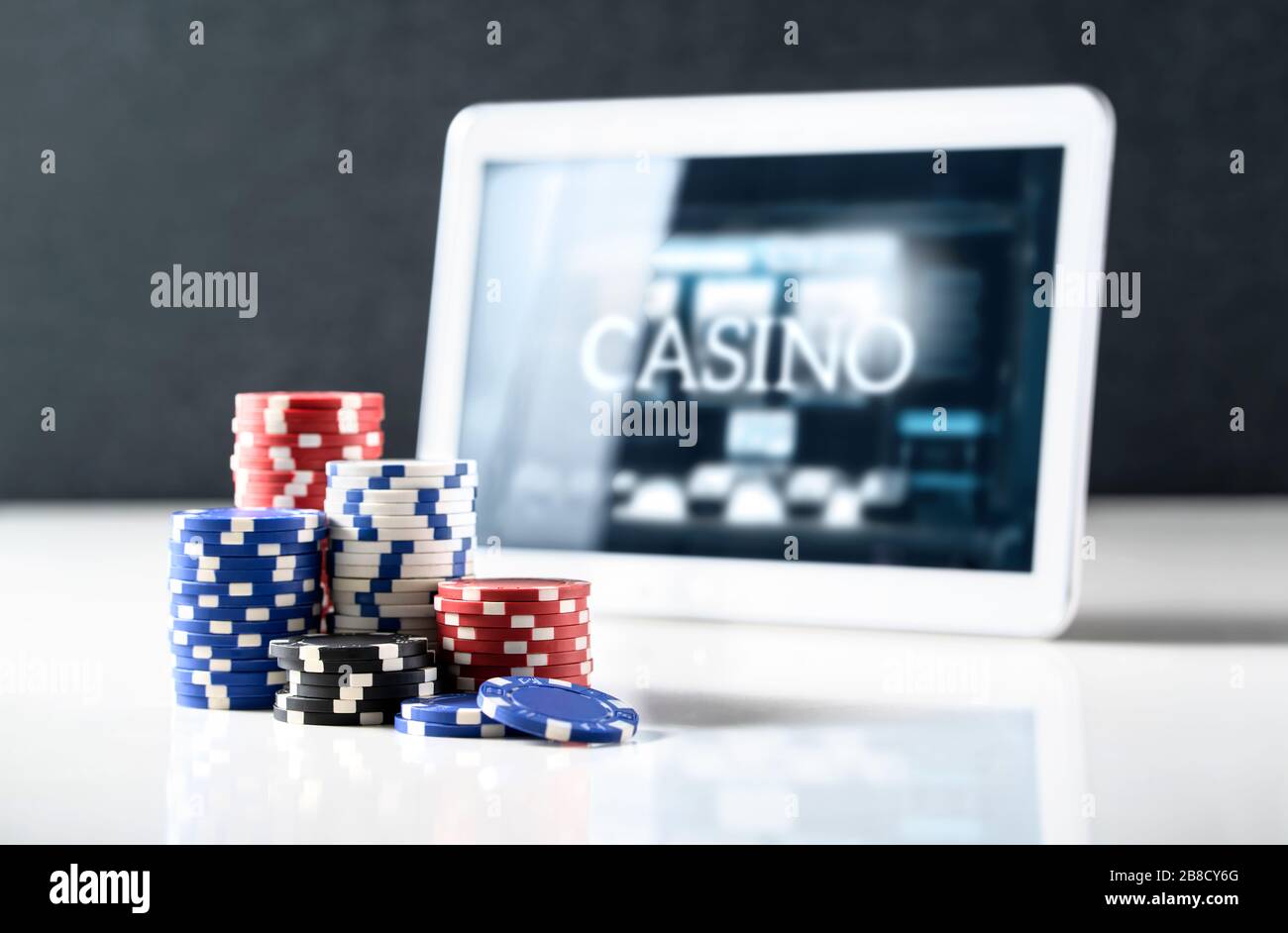 Il gioco d'azzardo online sul concetto di casinò mobile. Pila di chip poker e tablet con slot machine sullo schermo. Scommettere su internet e giocare a giochi digitali. Foto Stock