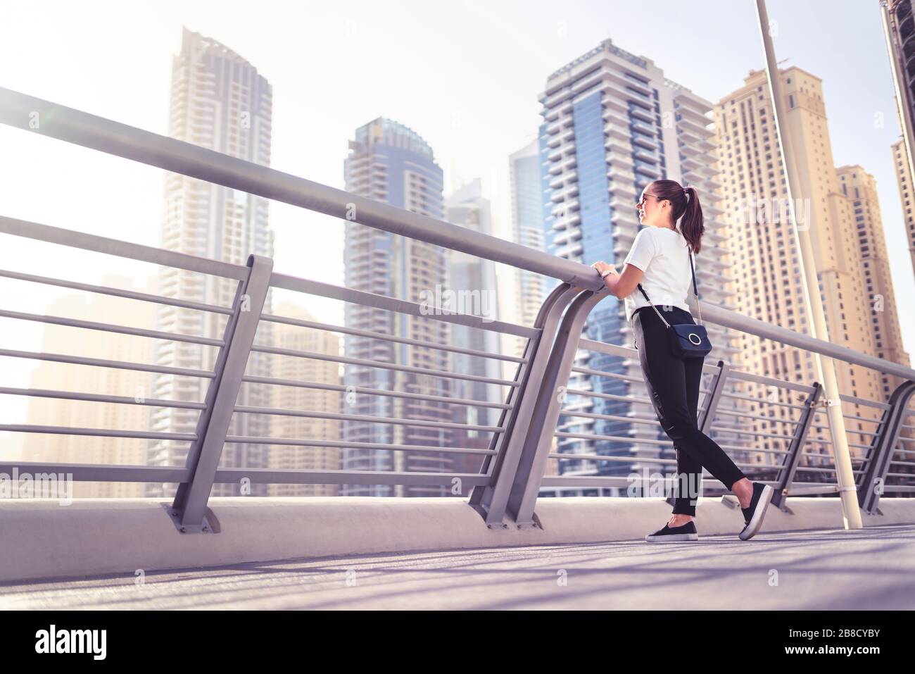 Elegante donna millenaria in città con outfit alla moda, jeans e borsa. Moderno stile di vita urbano di lusso. Happy hipster signora con stile informale strada. Foto Stock