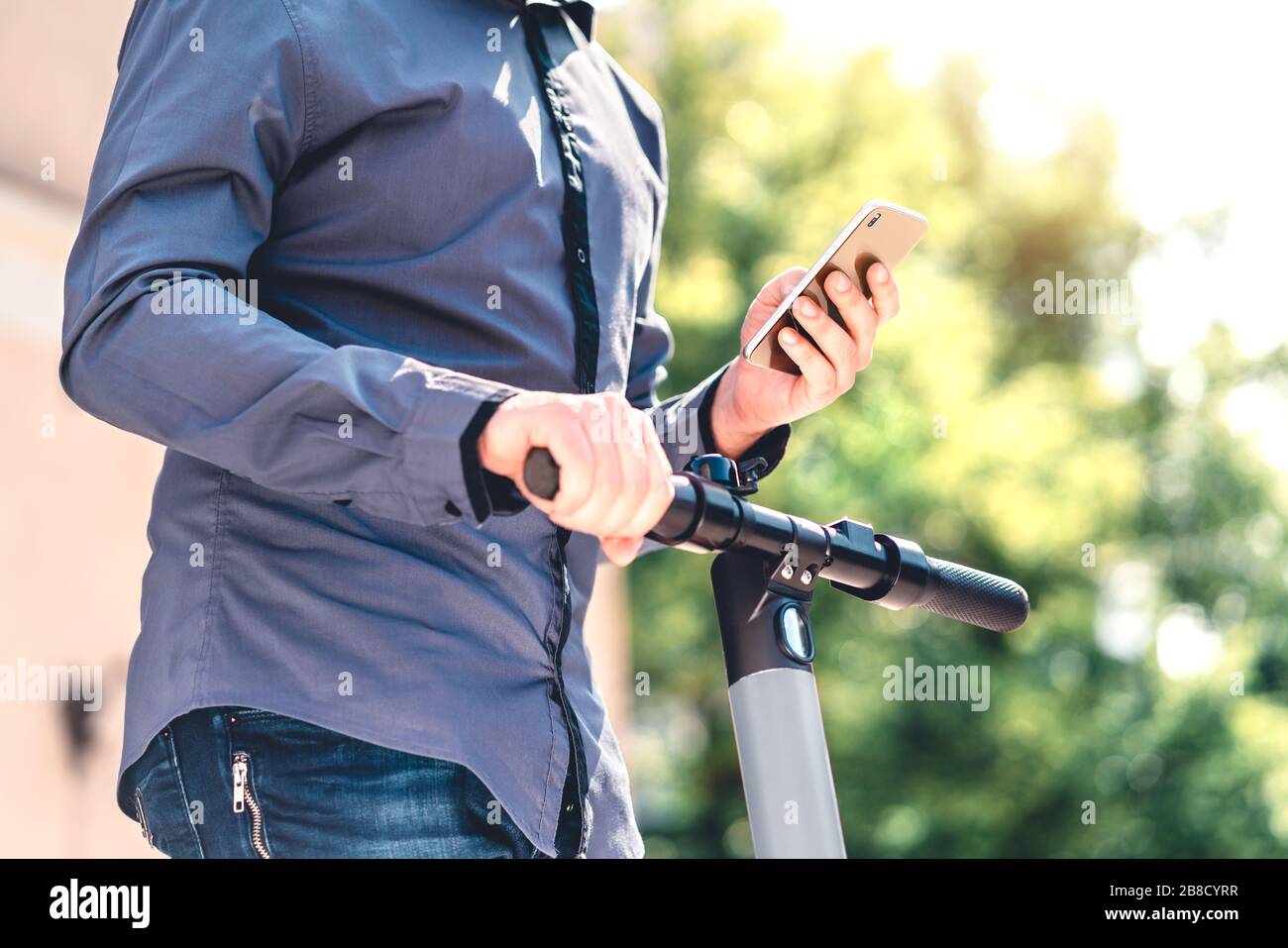 Scooter elettrico e telefono cellulare. Uomo d'affari che utilizza il servizio di noleggio veicoli con smartphone in città strada e parco. Giovane ragazzo millenario. Foto Stock