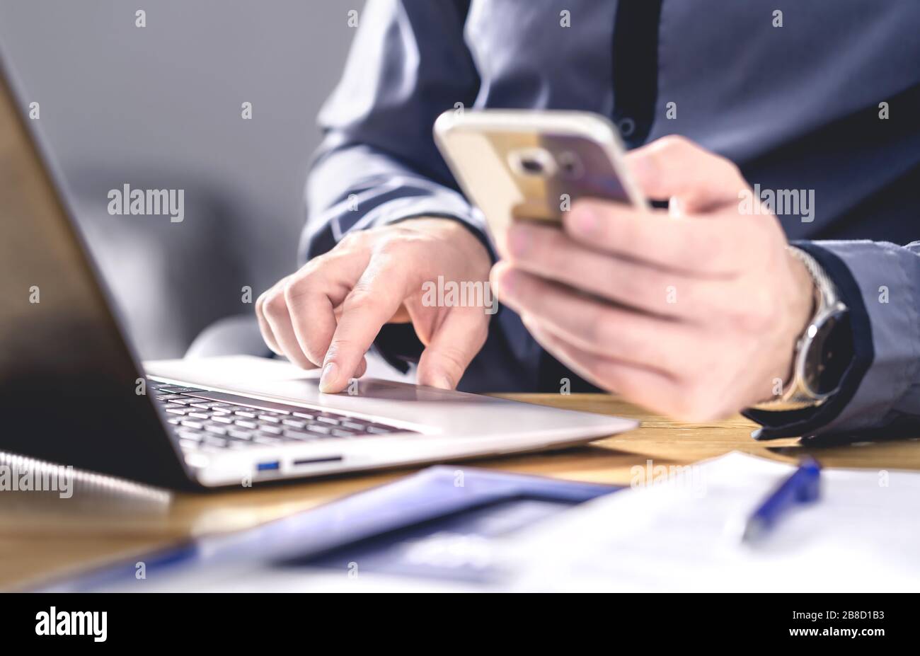 Multitasking e tecnologia mobile. Uomo d'affari occupato che usa il telefono e il laptop. Imprenditore che lavora duramente con smartphone e computer. Foto Stock