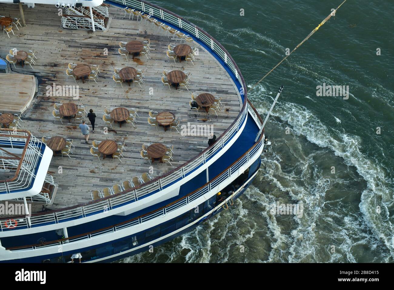 Vista in elicottero della poppa della nave da crociera con ponte di legno trainato via dal molo con forte corrente in acqua dai motori a piena forza Foto Stock