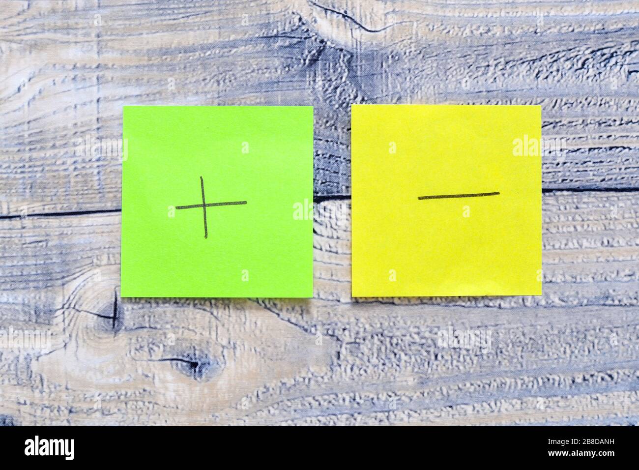 Due post su sfondo di legno con un simbolo più e meno su di esso Foto Stock