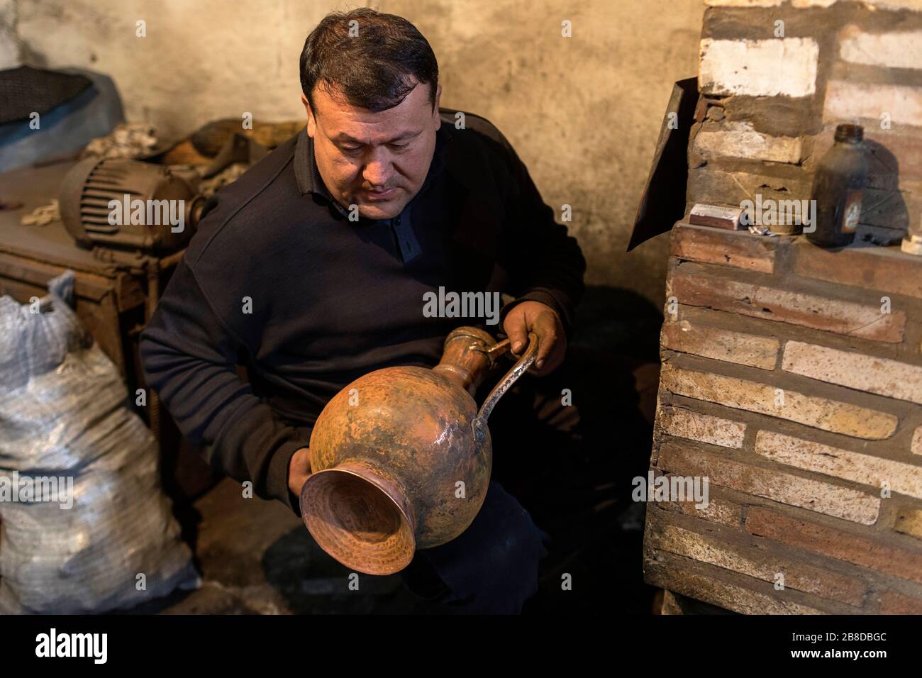 Artigiano locale dalla sua stufa che fa vasi metallici per cucinare il tè nella sua officina, Khiva, Uzbekistan Foto Stock