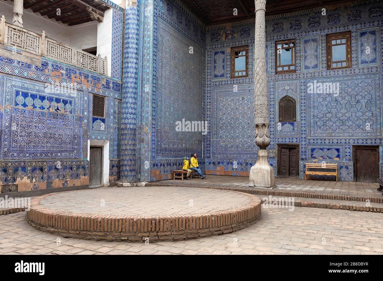 Madre e figlio seduti sulla panchina nel cortile interno con colonne scolpite e piastrelle dipinte, Tosh-Khovli o Palazzo di Khan, Khiva, Uzbekistan Foto Stock