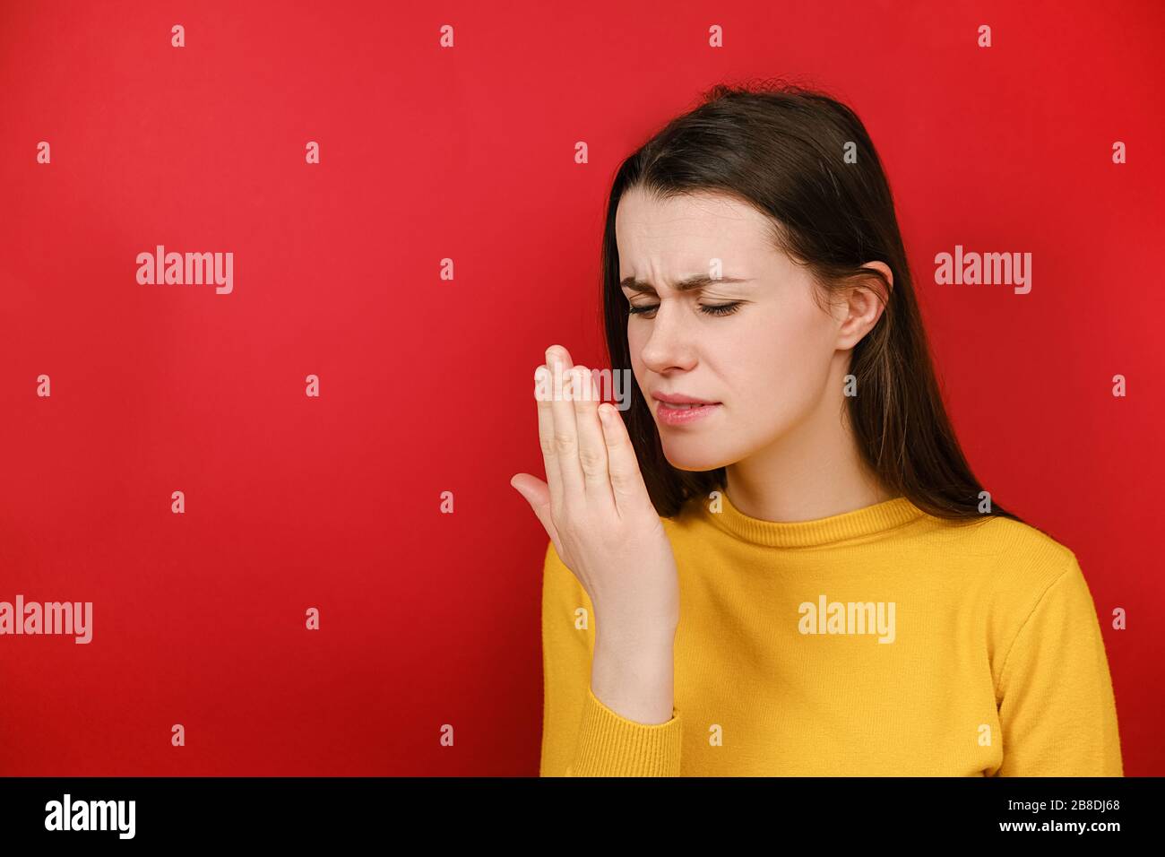 Malcontento giovane donna bruna controllare il respiro con la mano, odori qualcosa di orribile, pizzica il naso, rondine in disappunto, vestito in giallino maglione Foto Stock