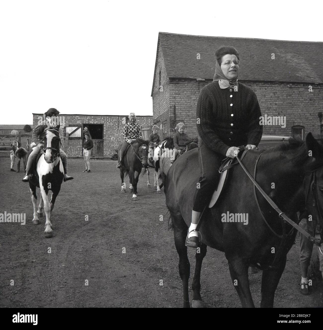 1963, storico, donna e bambini a cavallo in un cortile in una scuola di equitazione, Inghilterra, Regno Unito. Foto Stock