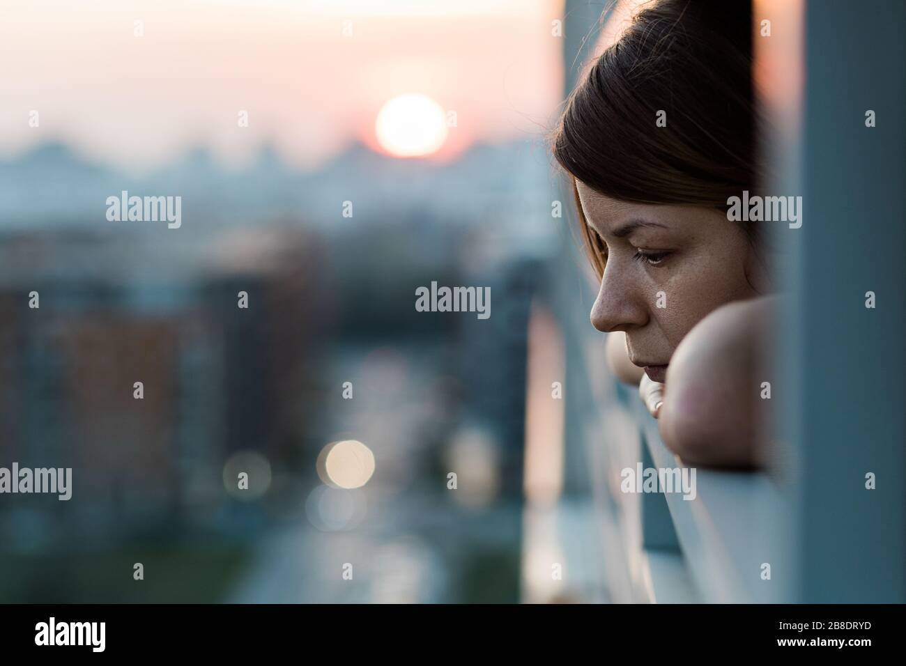 Giovane donna triste che guarda fuori attraverso il balcone di un edificio di appartamenti Foto Stock