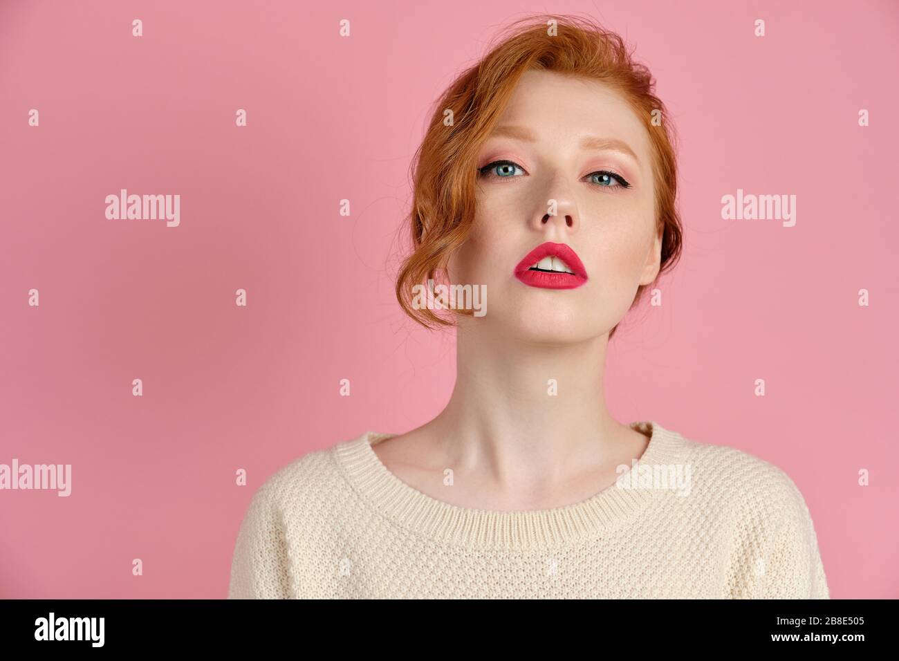 Ragazza dai capelli rossi con rossetto rosso e capelli raccolti guardando  la macchina fotografica, sollevando il mento su uno sfondo rosa Foto stock  - Alamy