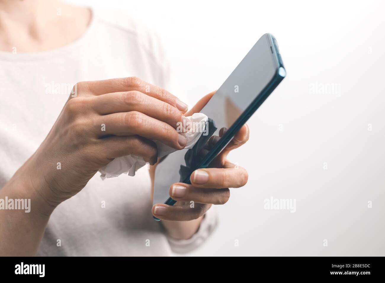 La donna disinfetta il telefono con alcool contro i batteri virali. Schermo dello smartphone con elaborazione antisettica. Foto Stock