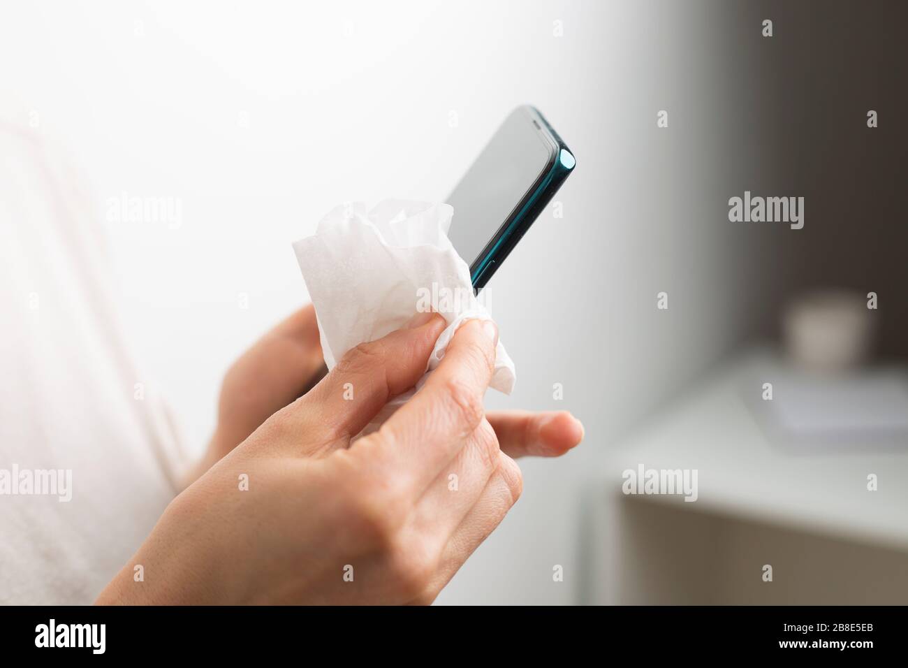 La donna disinfetta il telefono con alcool contro i batteri virali. Schermo dello smartphone con elaborazione antisettica. Foto Stock