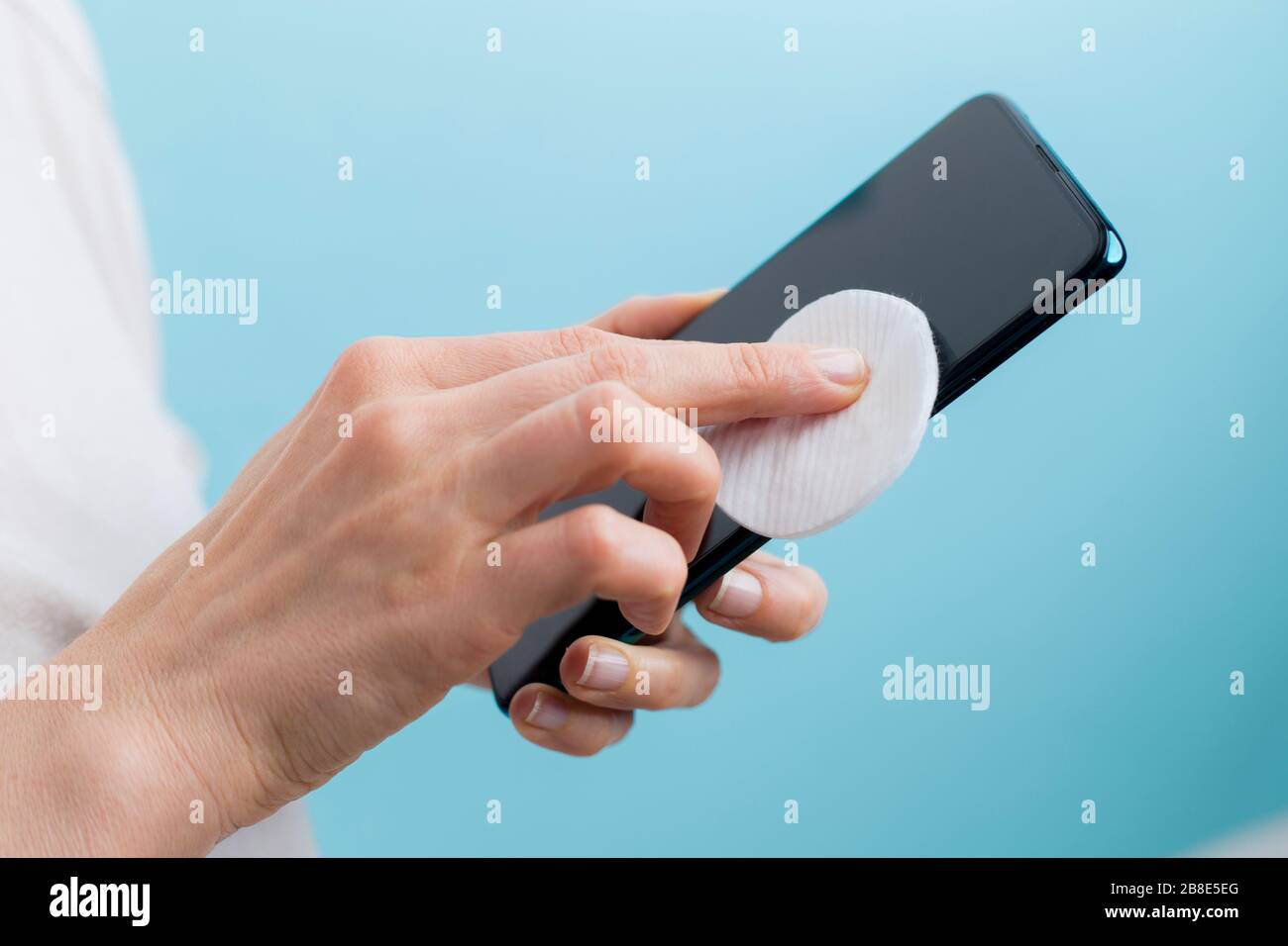 La donna disinfetta il telefono con alcool contro i batteri virali. Schermo dello smartphone con elaborazione antisettica. Foto Stock