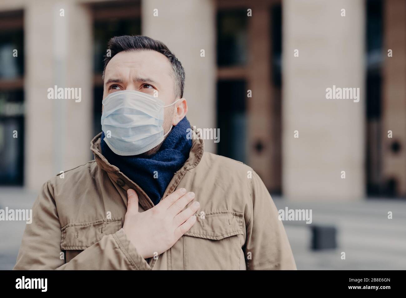 Il colpo esterno dell'uomo malato porta la maschera medica contro i virus, ha shortness di alito e tosse, ritiene malessere, protegge da coronavirus, si preoccupa circa h Foto Stock