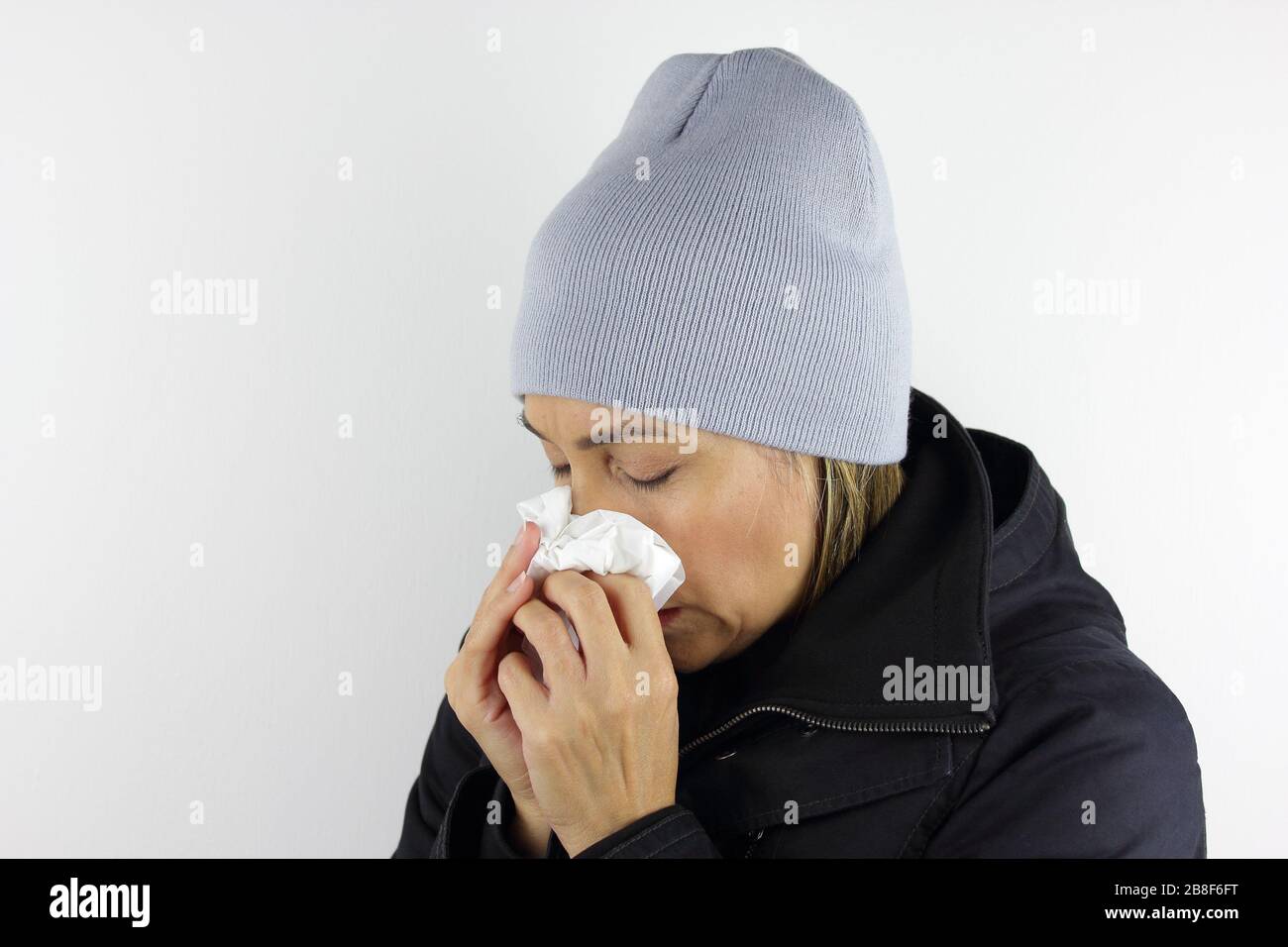 Donna malata che indossa un berretto e che usa un tessuto per starnutire e soffiare il naso. Foto Stock