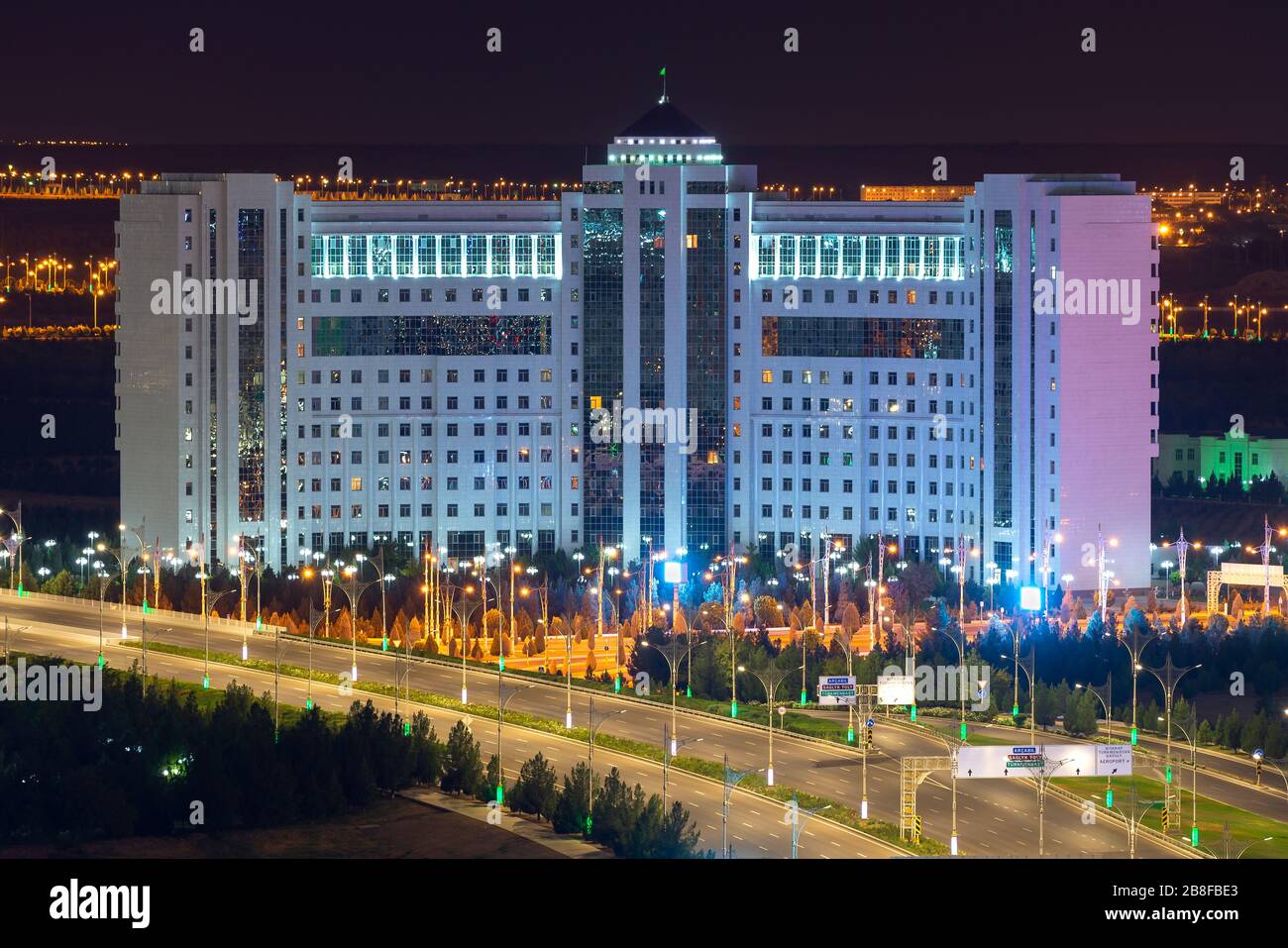 Imponente edificio curvo in marmo bianco ad Ashgabat, Turkmenistan. Empty Archabil Highway in primo piano con bei pali di lampada in una città esotica. Foto Stock