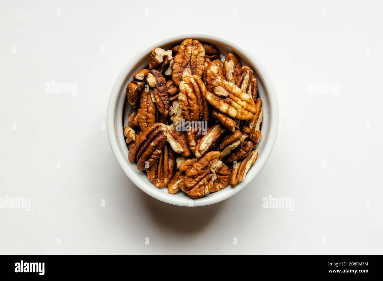 Una piccola ciotola bianca di deliziose noci di noci salate salate, isolate su sfondo bianco, da vicino Foto Stock