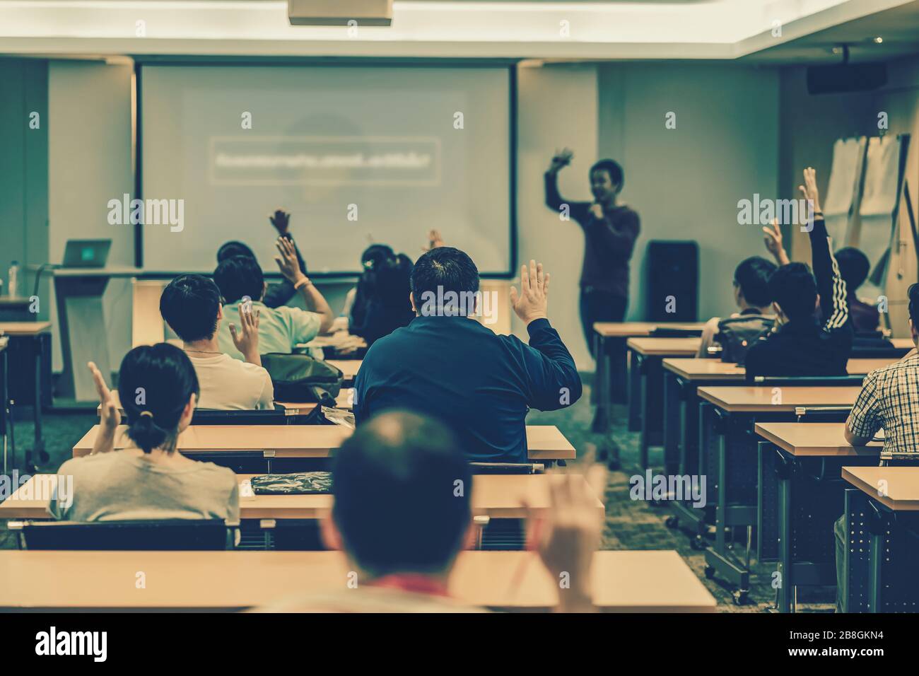 Vista posteriore del pubblico in risposta mano per rispondere alla domanda nella sala riunioni o nella sala conferenze sopra l'altoparlante asiatico sul palco, seminario Foto Stock