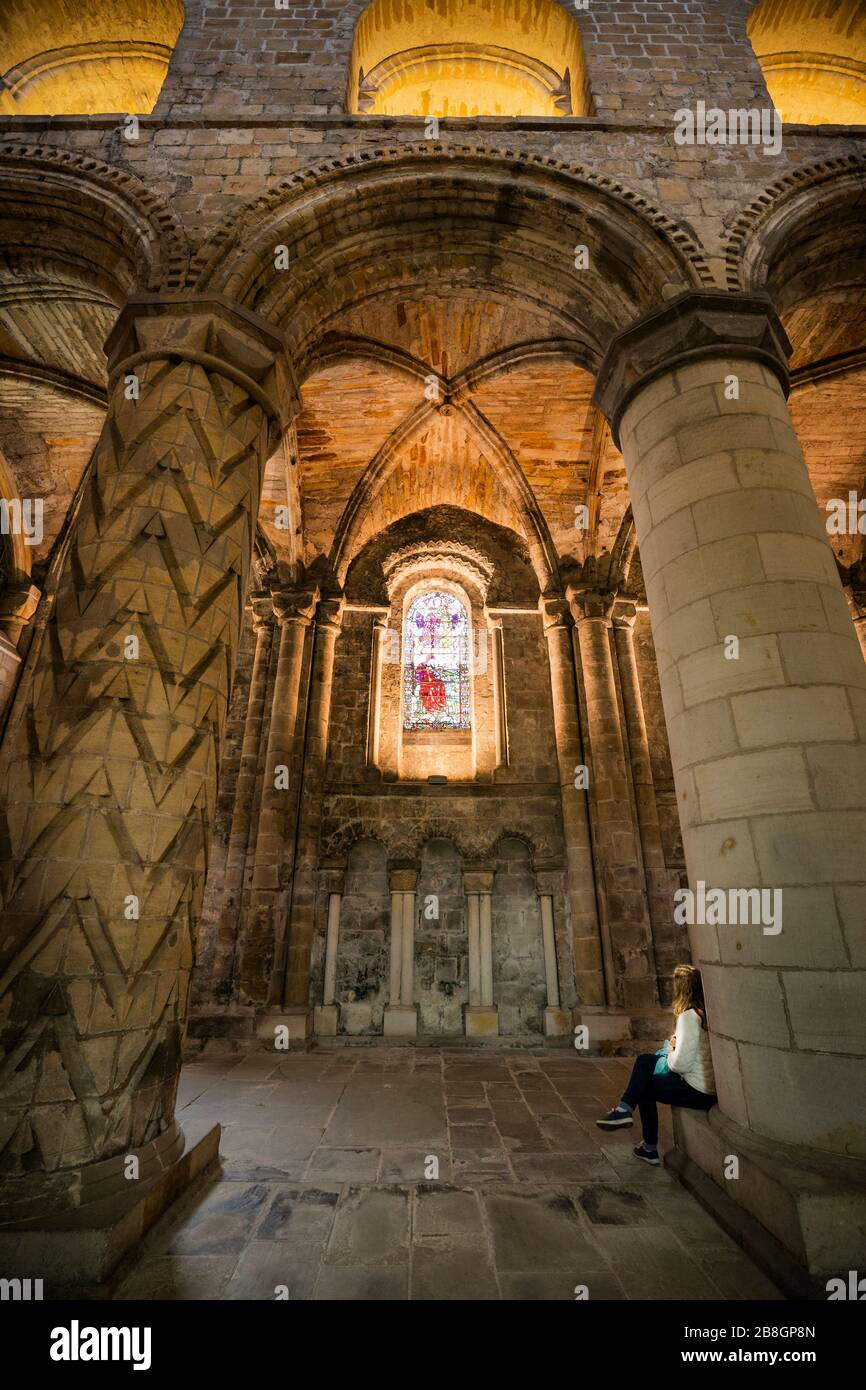 Il turista femminile siede alla base di una colonna scolpita ammirando le vetrate all'interno dell'Abbazia di Dunfermline, una chiesa della parrocchia di Scozia, Dunfermline; Foto Stock