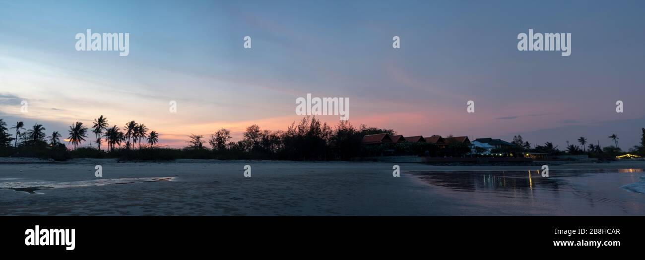 Panorama, alberi di cocco e alberi che separano la spiaggia 'Chao Satran' e la strada, cielo la sera dopo il tramonto Foto Stock