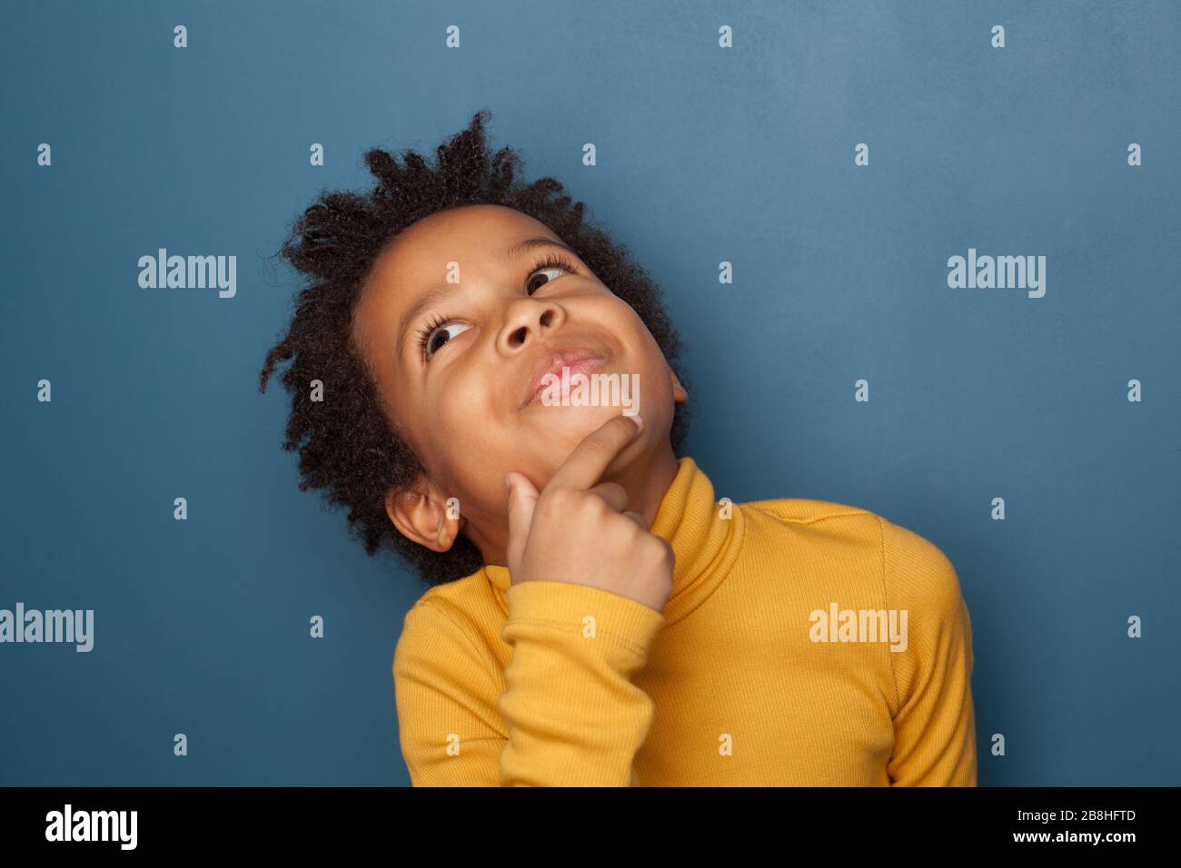 Piccolo bambino nero ragazzo pensando e guardando su su sfondo blu Foto Stock