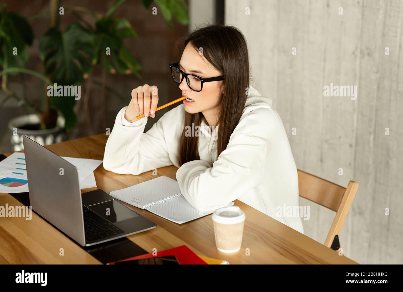 Ragazza con occhiali analizza lavoro, tenendo matita Foto Stock
