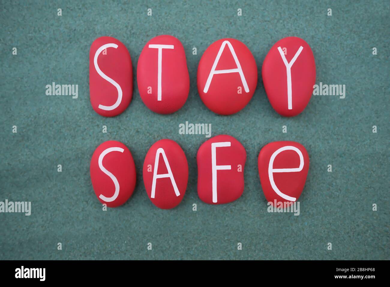 Stay Safe, slogan creativo composto con lettere di pietra dipinta di colore rosso su sabbia verde Foto Stock