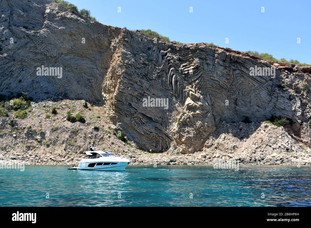 Barca ancorata sotto le scogliere vicino Punta grossa, Ibiza, Spagna Foto Stock