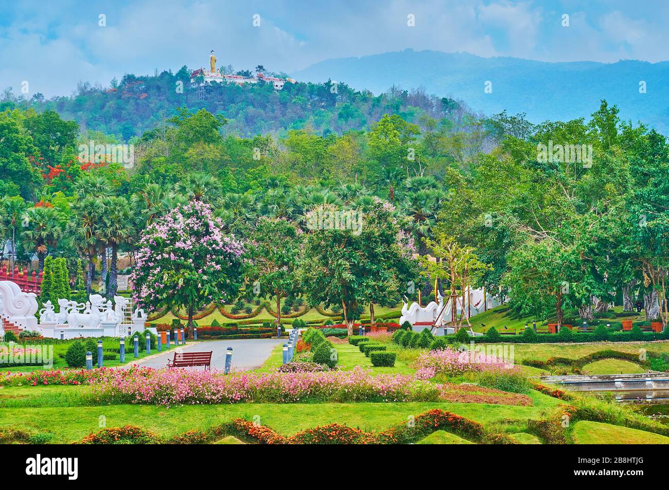 Godetevi i vicoli verdi del parco Rajapruek con colorati aiuole, alberi in fiore, cespugli topiari e Wat Phra That Doi Kham tempio in cima alla montagna Foto Stock
