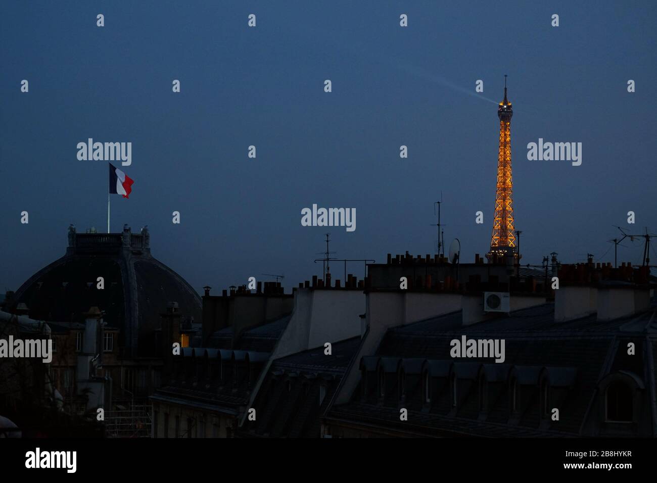 Notte a Parigi, una bandiera francese vola sopra la camera del Cercle National des armées, con un fascio di luce illuminato sulla Torre Eiffel contro il cielo blu profondo Foto Stock