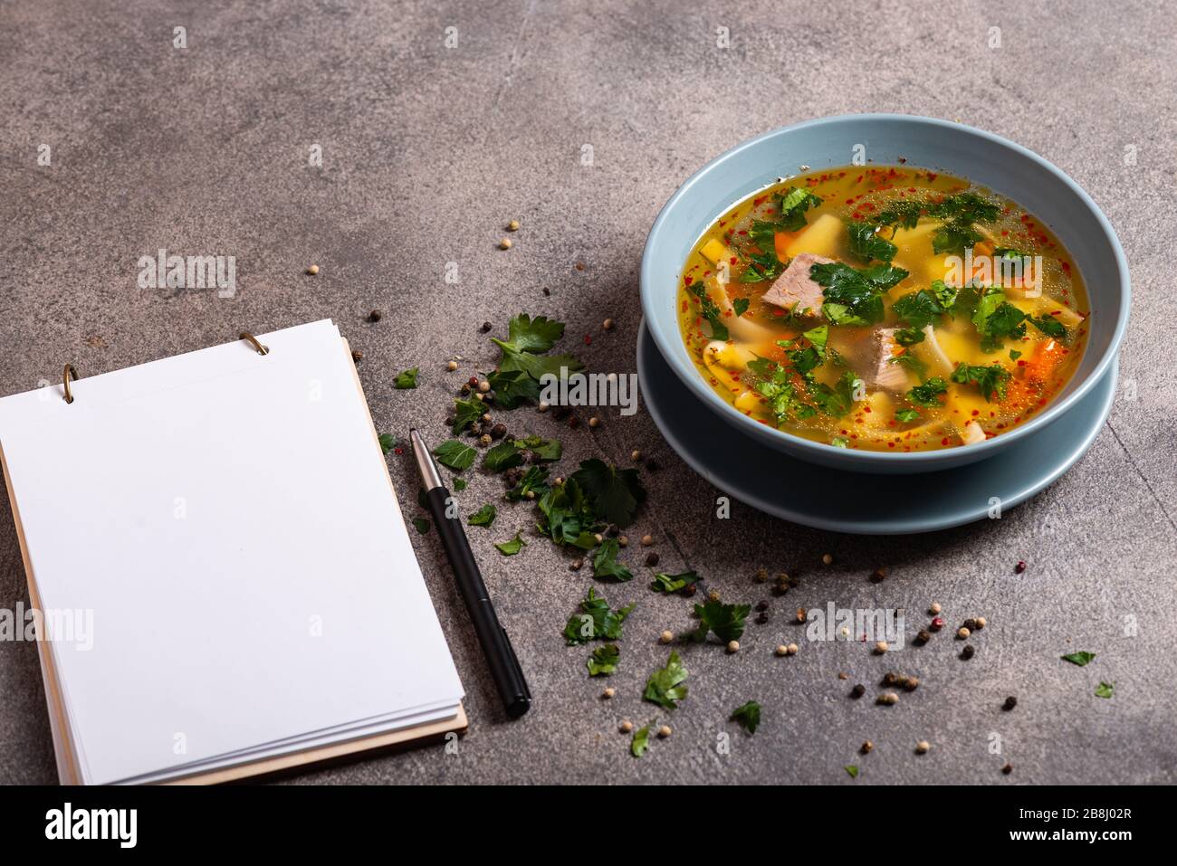 Deliziosa zuppa piccante con manzo e spaghetti su sfondo grigio. Un libro per la scrittura delle ricette si trova su una tabella. Primo piano. Foto Stock