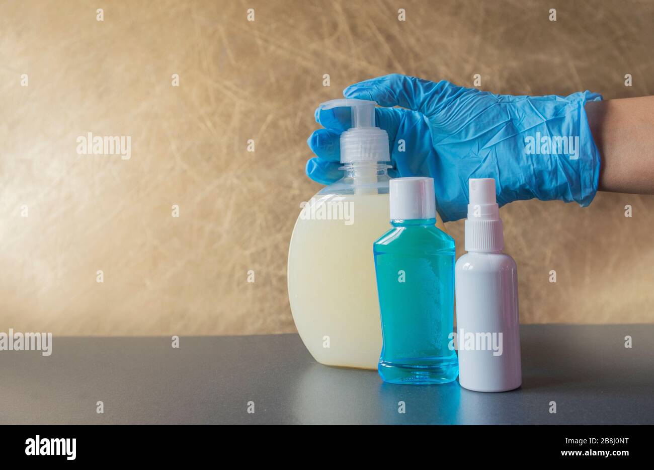 ragazza tiene in mano bottiglie con un antisettico con sapone liquido per la pulizia contro i batteri in guanti di gomma blu Foto Stock