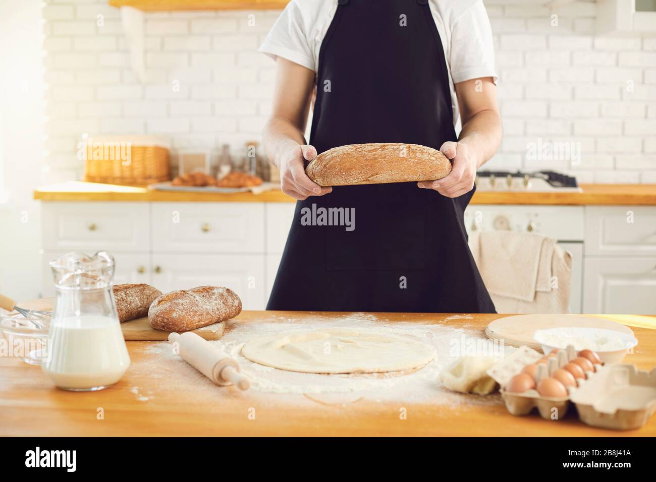 L'uomo bearded di Baker tiene nelle sue mani il pane fresco che sta in piedi nella cucina. Foto Stock
