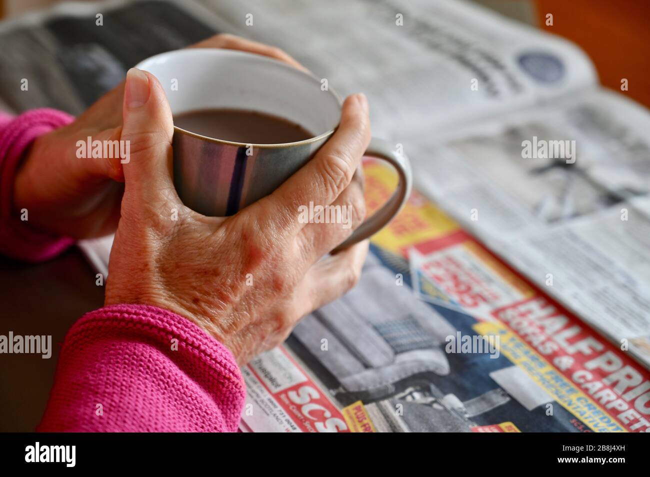 Primo piano di una donna anziana che tiene una tazza di caffè e legge la carta. Foto Stock