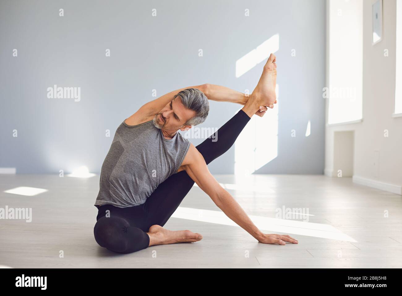 Uomo yoga. Un uomo sta praticando l'equilibrio dello yoga in una stanza grigia. Foto Stock