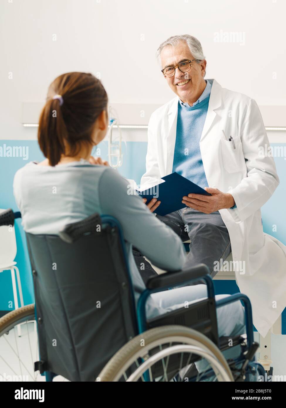 Medico sicuro che visita un paziente paraplegico in sedia a rotelle presso l'ospedale Foto Stock