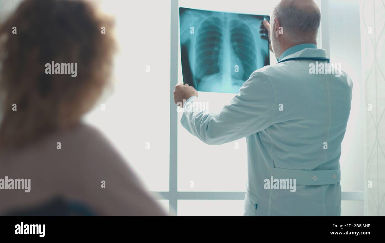 Medico senior professionista che controlla la radiografia di un paziente in clinica, la donna lo sta ascoltando Foto Stock