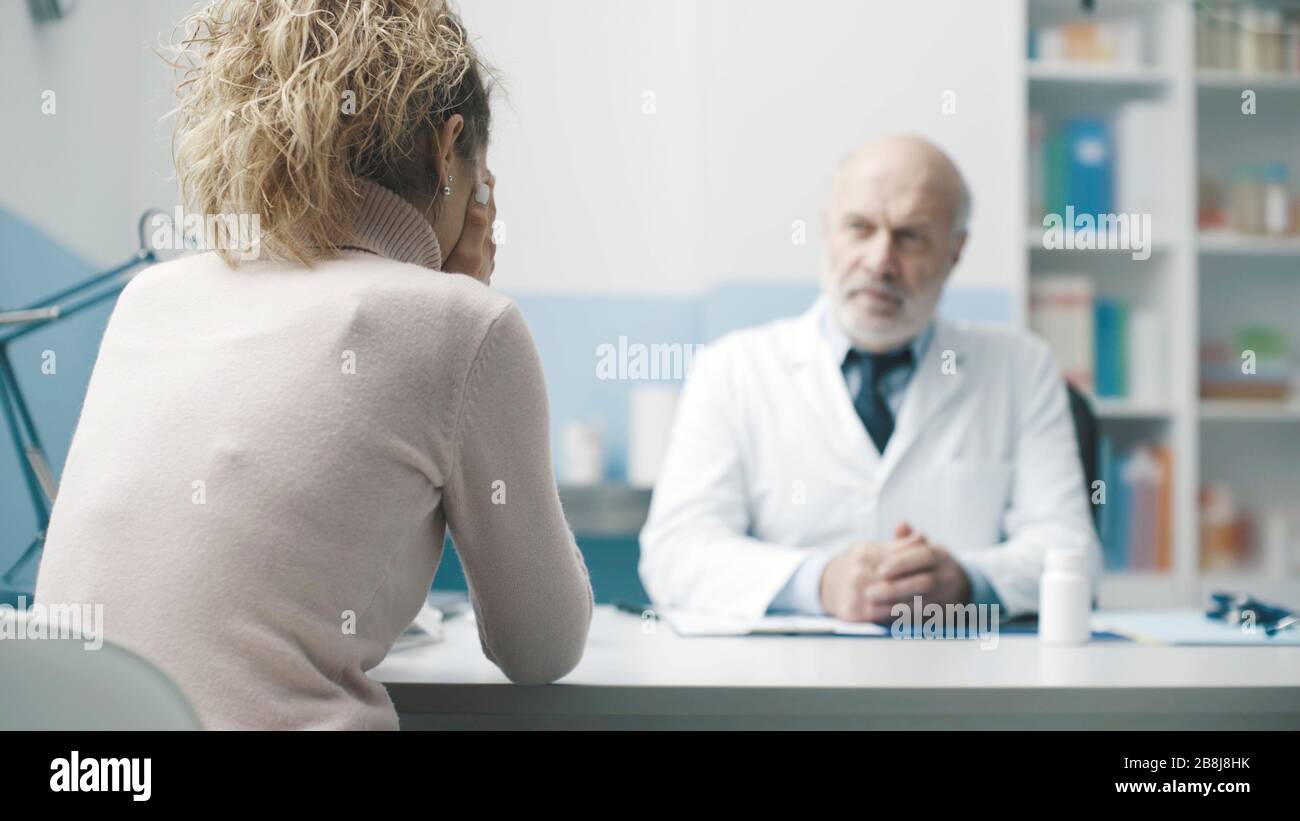 Dottore che dà cattive notizie ad un paziente, la donna sta piangendo con la testa in mano Foto Stock