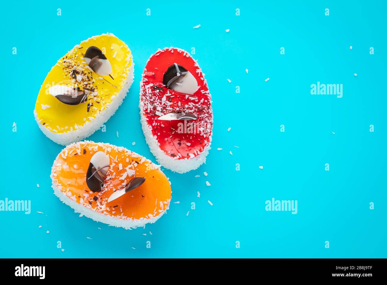 Torte multicolore con scaglie di cocco su sfondo blu. Dessert fatti in casa, cibi dolci ad alta caloria. Design laconico, concetto di umore divertente. Testo, c Foto Stock