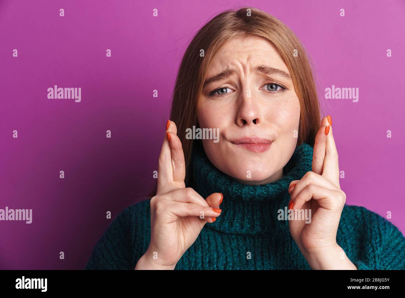 Foto di giovane donna nervosa che posa isolato su sfondo muro viola con le dita fiduciose si prega di attraversare gesto. Foto Stock
