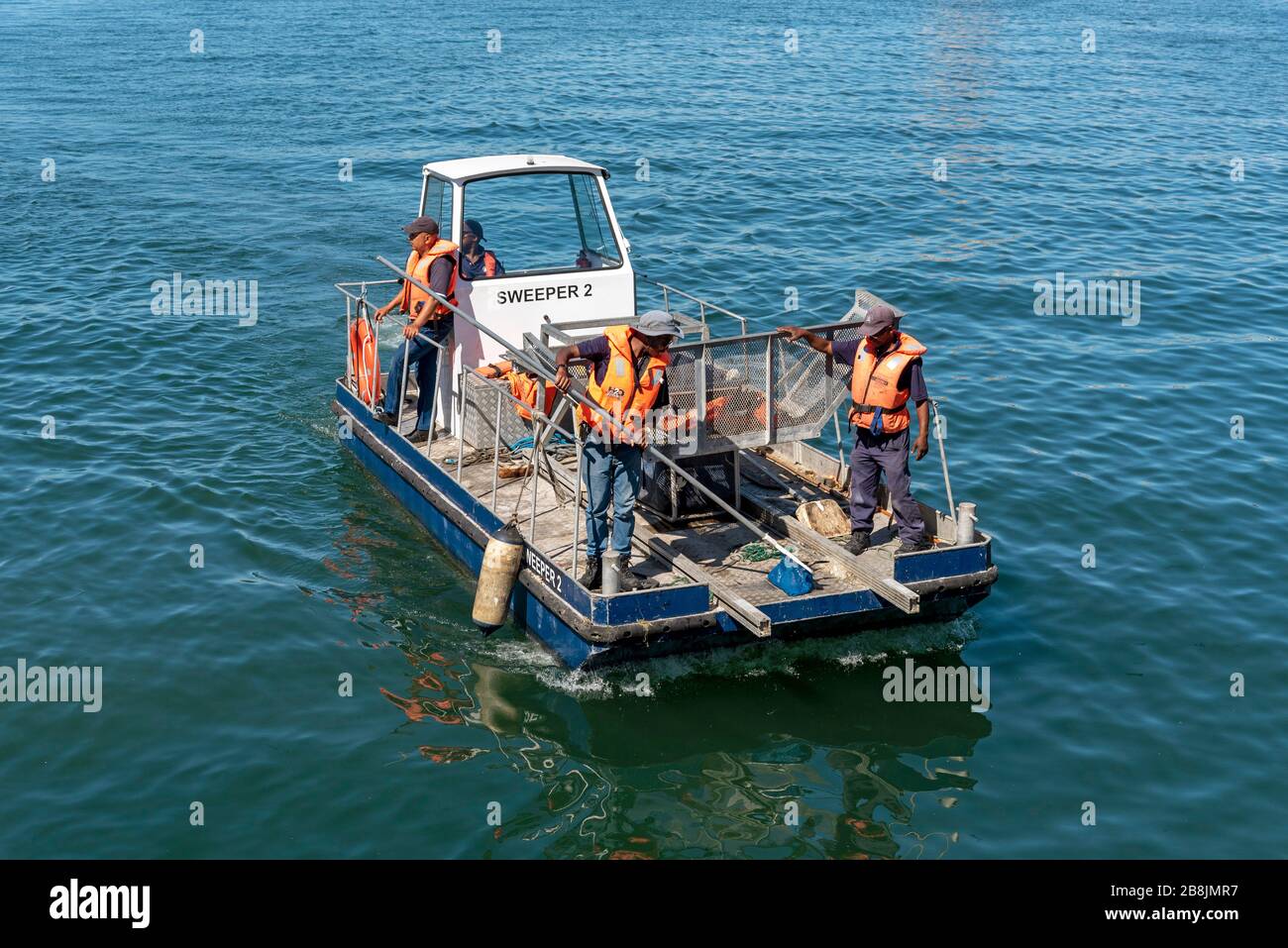 Città del Capo, Sudafrica.. Lavoratori di un porto e di una nave di pulizia del porto che raccolgono rifiuti, detriti e vegetazione acquatica dall'acqua Foto Stock