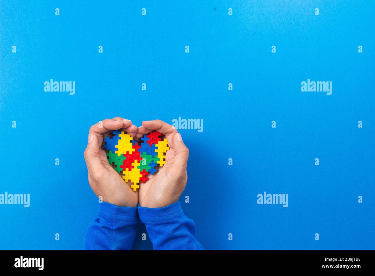 Concetto del giorno di consapevolezza di autismo del mondo. Le mani del bambino tengono il cuore colorato del puzzle su sfondo blu Foto Stock