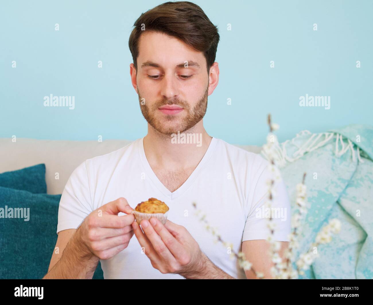 Giovane caucasico in una camicia bianca che tiene un primo piano di muffin fatti in casa. Foto Stock