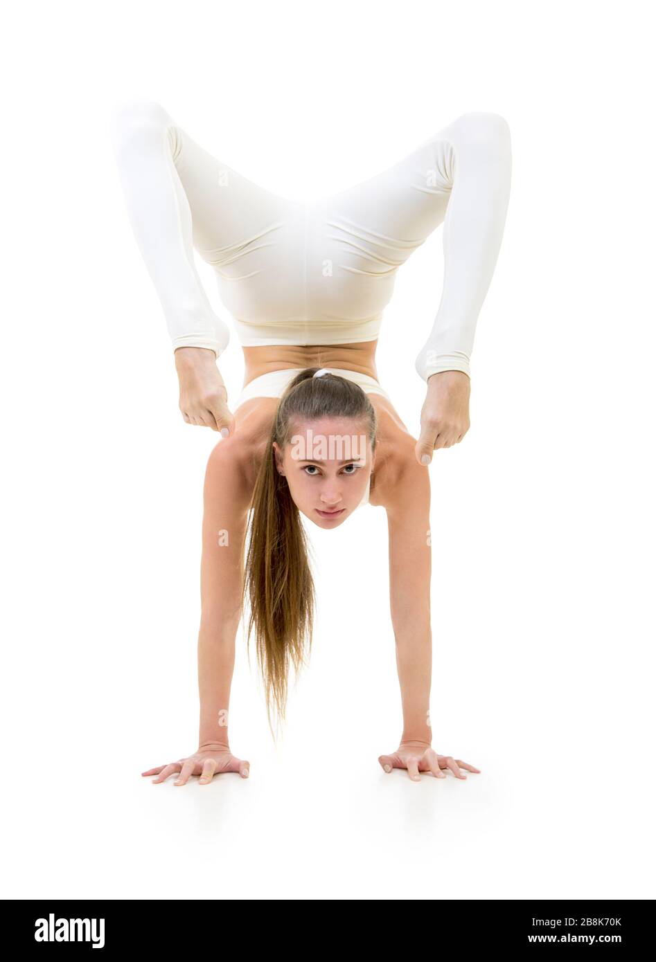 Una giovane donna in tuta bianca esegue elementi acrobatici e yoga. Studio girato su sfondo bianco. Immagine isolata. Foto Stock