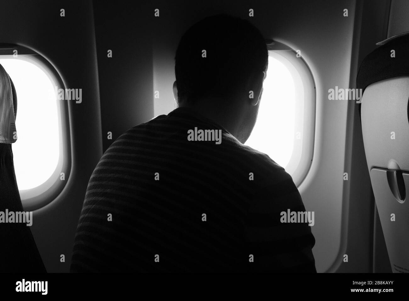 Una vista posteriore di un uomo seduto su un aereo, guardando la vista dalla finestra dell'aereo. Foto Stock