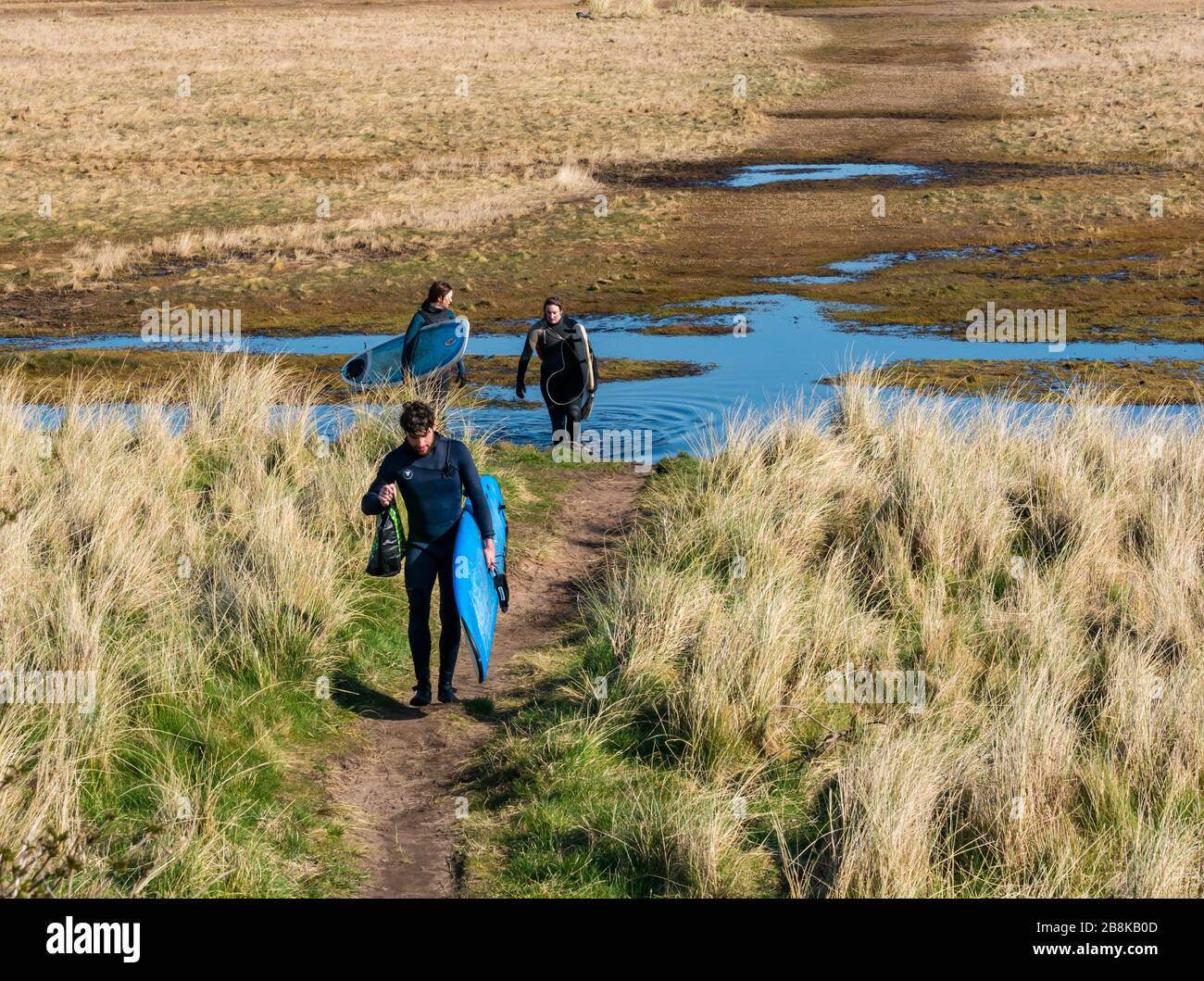 John Muir Country Park, East Lothian, Scozia, Regno Unito. 22 marzo 2020. UK Weather: Il sole di primavera permette alle persone di godere l'aria aperta nonostante le misure di distanza sociale. Un ritorno di gruppo dal surf a Belhaven Bay Foto Stock