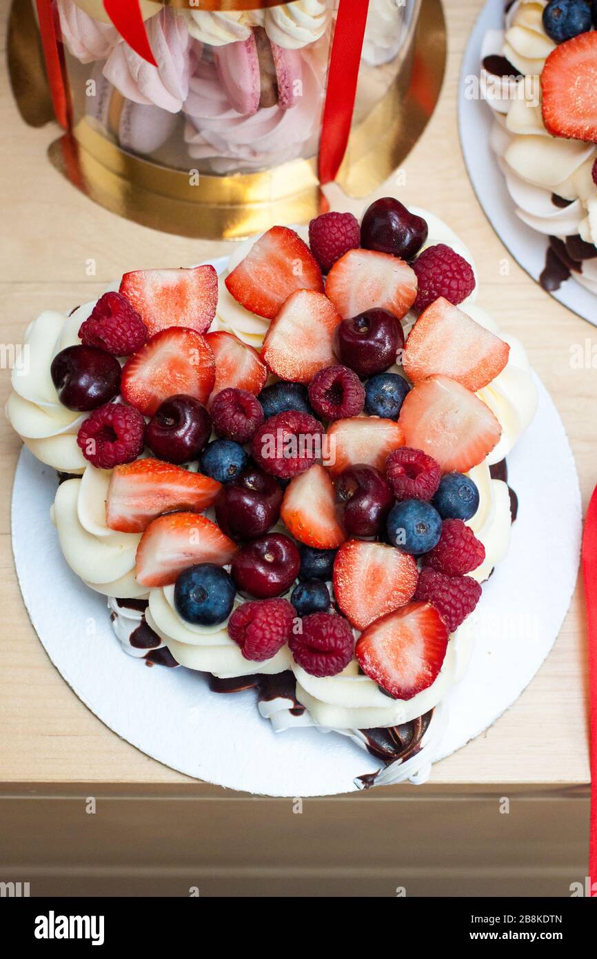 Torta Pavlova con fragole fresche, ciliegie, mirtilli e lamponi, cioccolato fuso e panna montata. Foto Stock