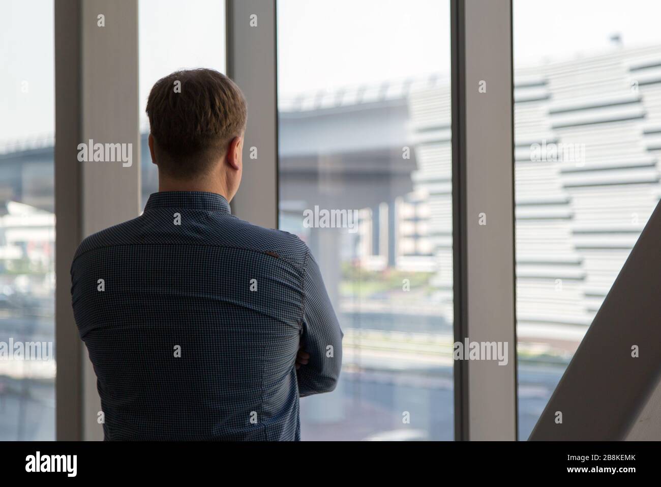 Un uomo di 40-45-anno in una camicia blu a quadri si pone nel corridoio posteriore dell'ufficio in mezzo ad una grande finestra. Foto Stock