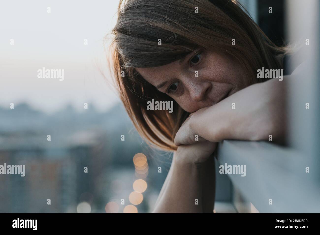 Giovane donna triste che guarda fuori attraverso il balcone di un edificio di appartamenti Foto Stock