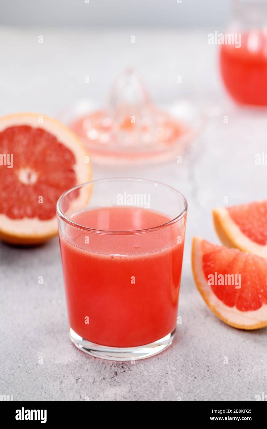 Un bicchiere di succo di pompelmo appena fatto e fette di frutta fresca su uno sfondo di cemento chiaro. Bevanda sana e dietetica. Primo piano Foto Stock