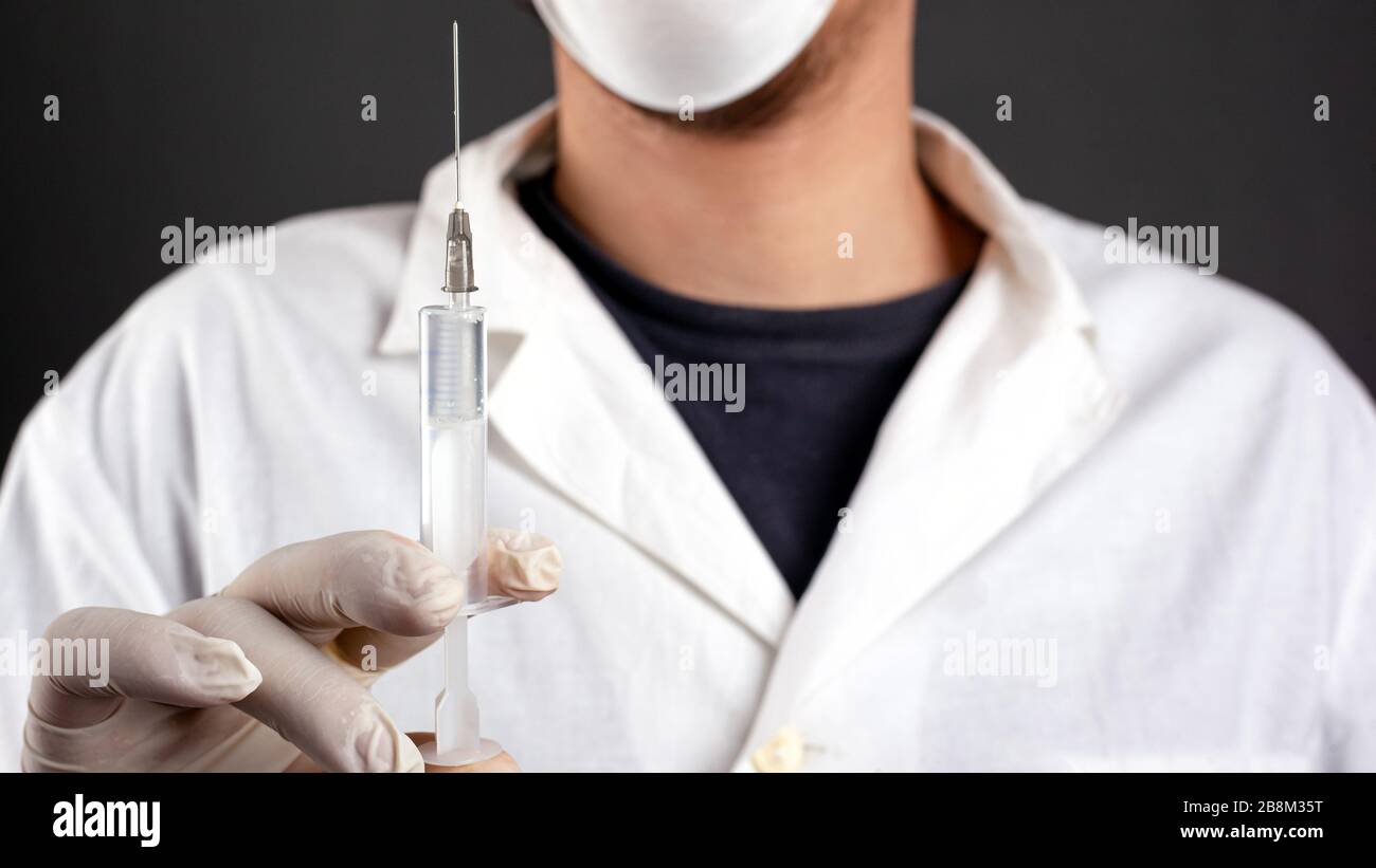 medico in un mantello bianco con guanti e una maschera medica tenere una siringa con il trattamento medico prevenzione della malattia vaccinazione contro le vie respiratorie virali Foto Stock